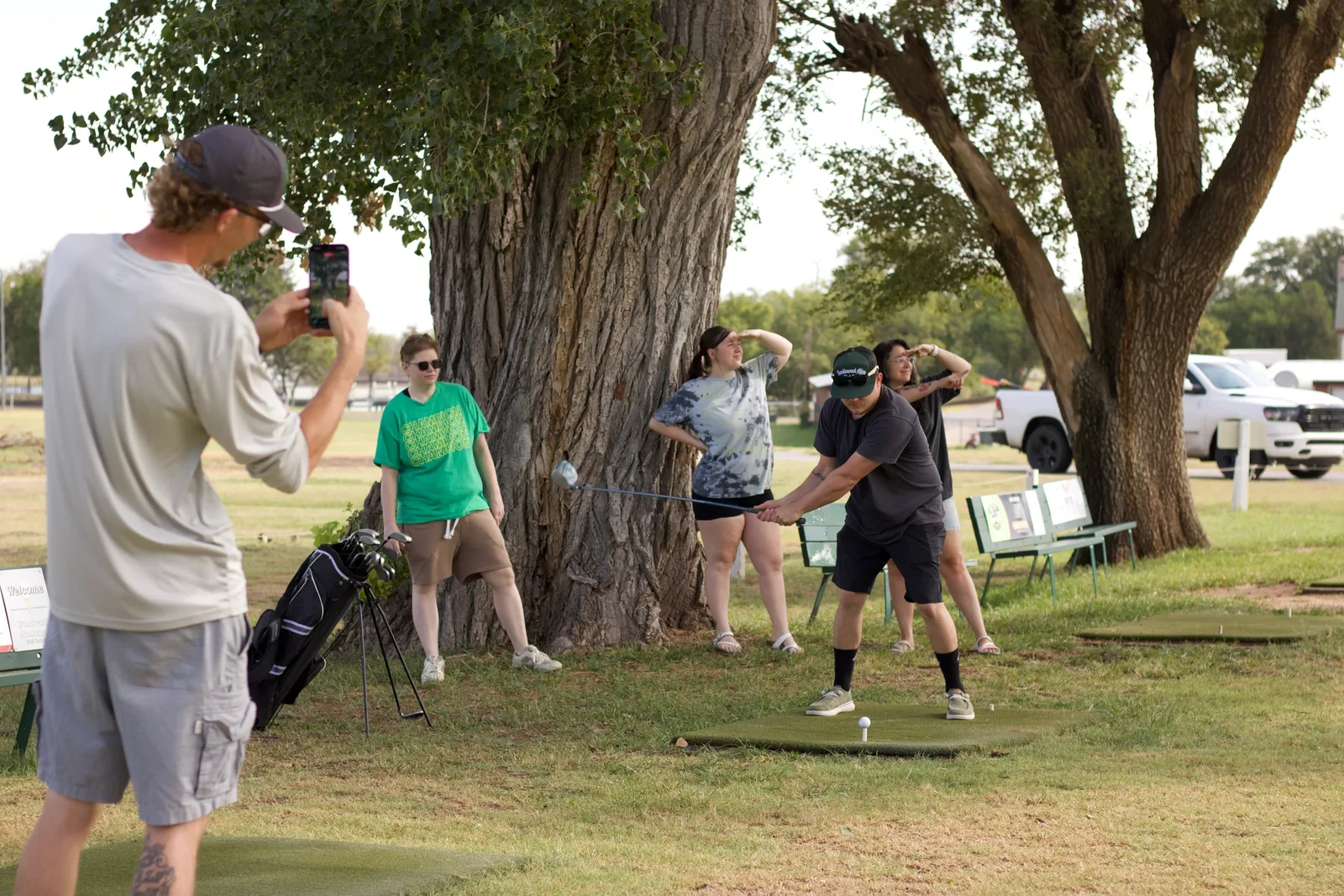 A team on a Stampede hunt: one player films while the others strike a pose under a big tree in a park.